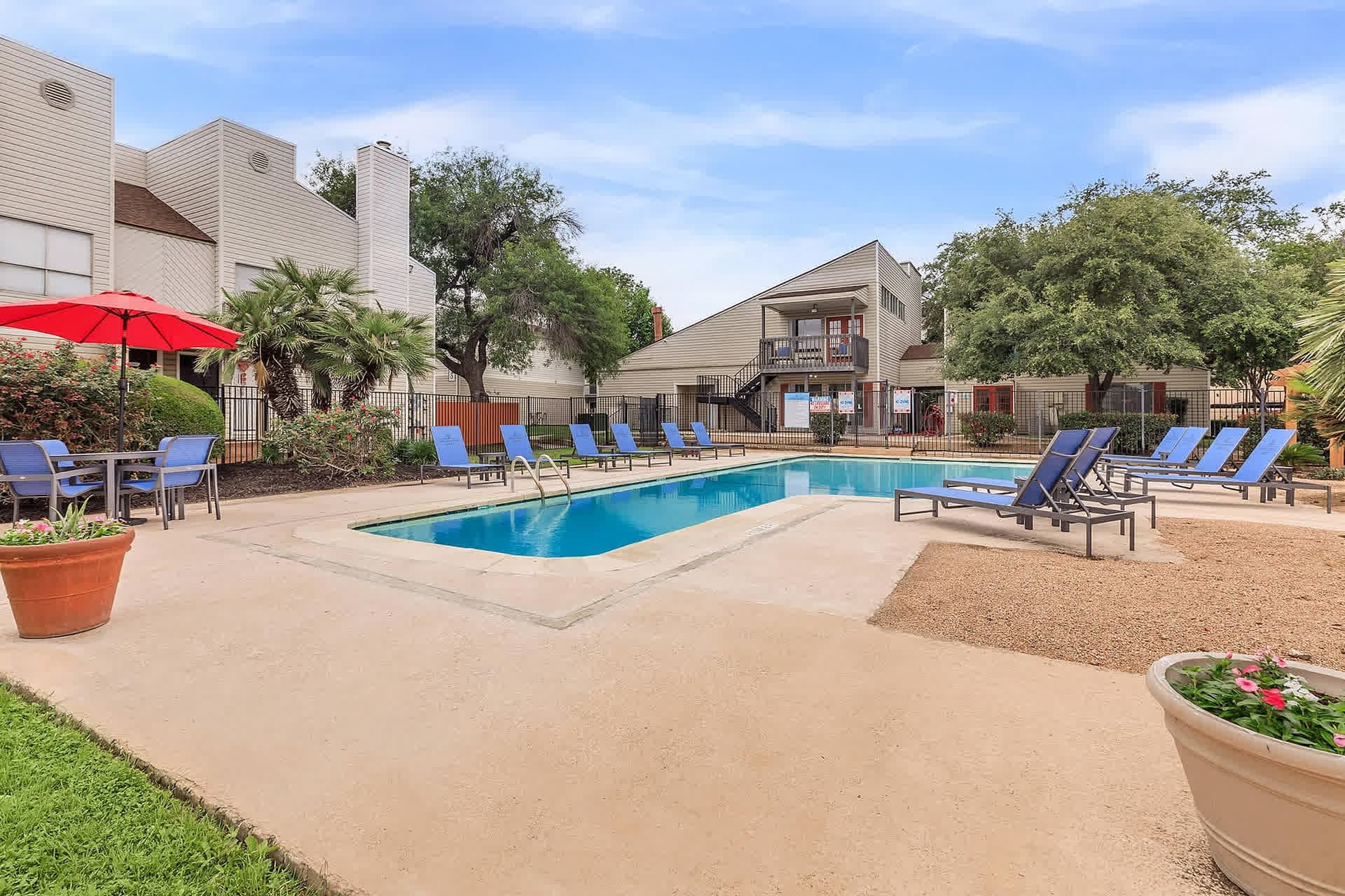 Swimming pool on a sunny day with blue loungers and a red patio umbrella